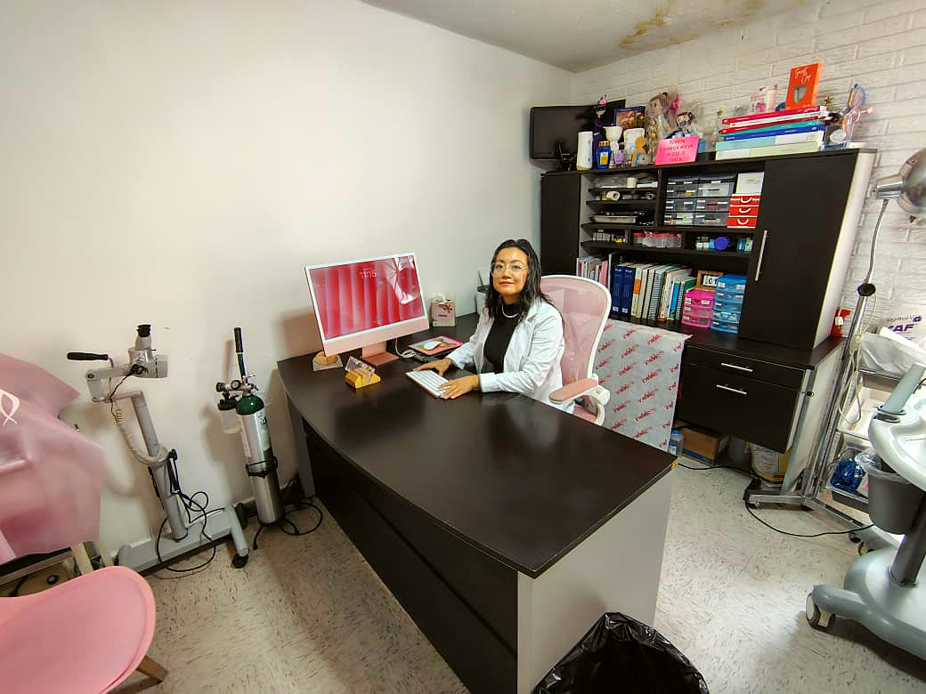 La Dra. Karla Román en su escritorio, con el consultorio completo detrás